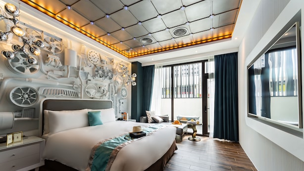 Une chambre d’hôtel moderne avec un grand lit, un plafond orné de luminaires circulaires, une grande fenêtre avec des rideaux et une vue sur la ville.