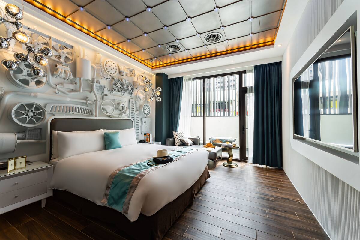 Una habitación de hotel moderna con una cama grande, un techo con lámparas circulares, un ventanal con cortinas y vistas a la ciudad.