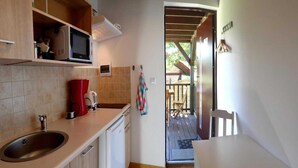 A compact kitchen with a sink, microwave, and a small refrigerator. A red kettle and a toaster are on the counter. A chair and a table are visible in the adjacent dining area. - Bungalow in Kolczewo with parking space (Kolczewo)