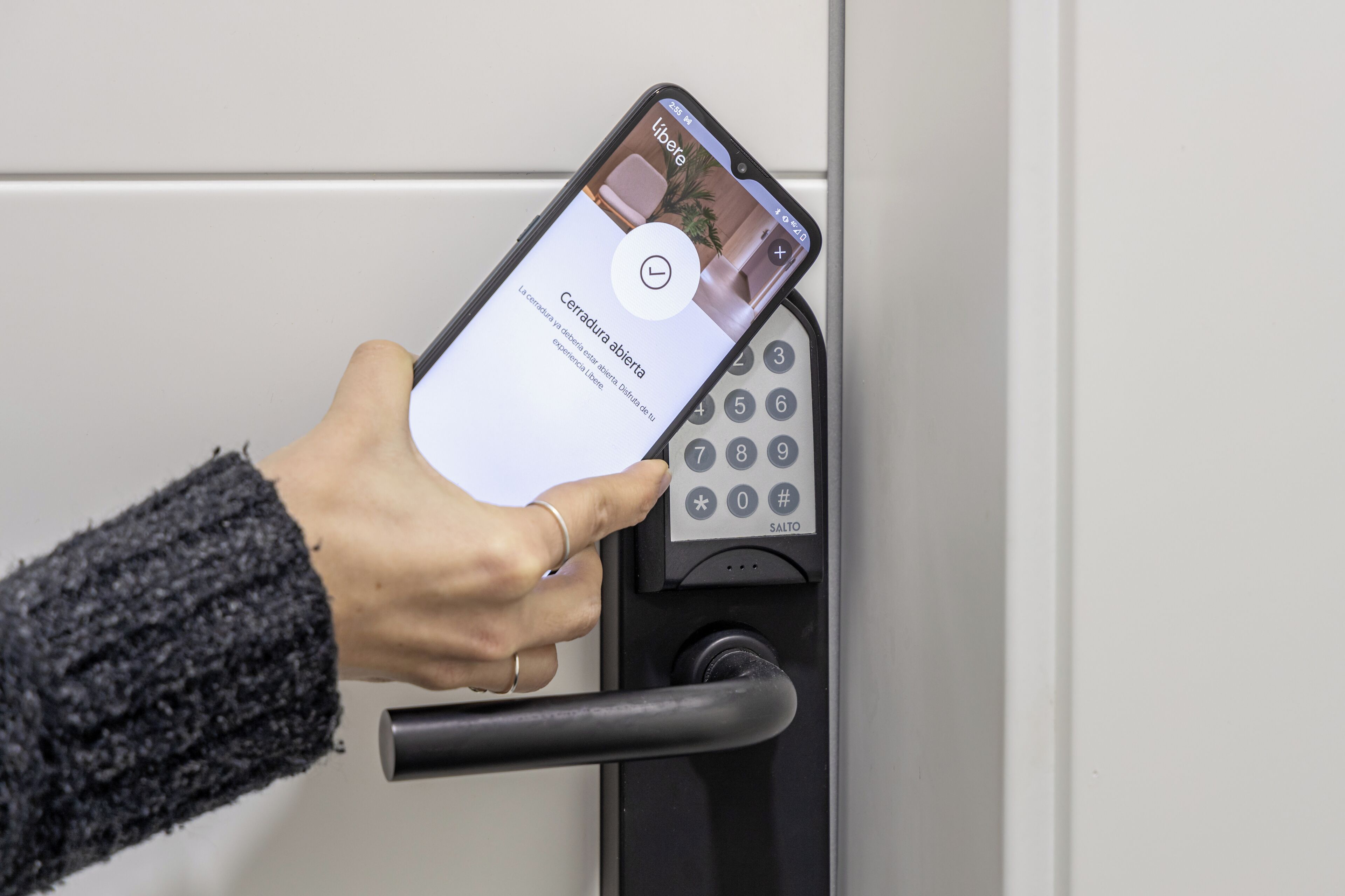 A hand using a smartphone to interact with a keypad lock.