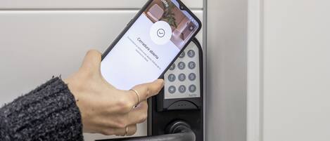 A hand using a smartphone to interact with a keypad lock.