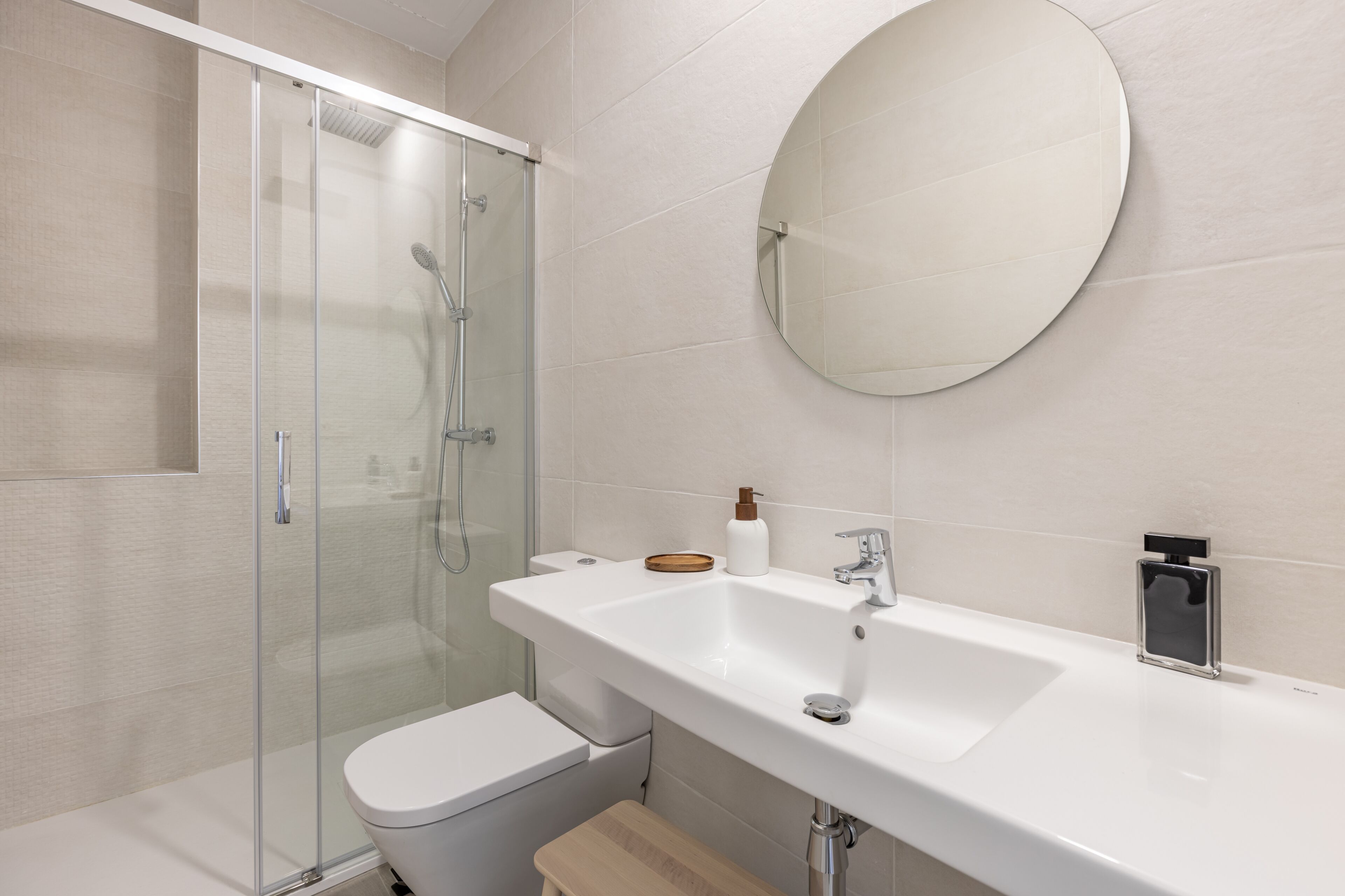 Un baño moderno con cabina de ducha de vidrio, un lavabo blanco con espejo y un banco de madera.