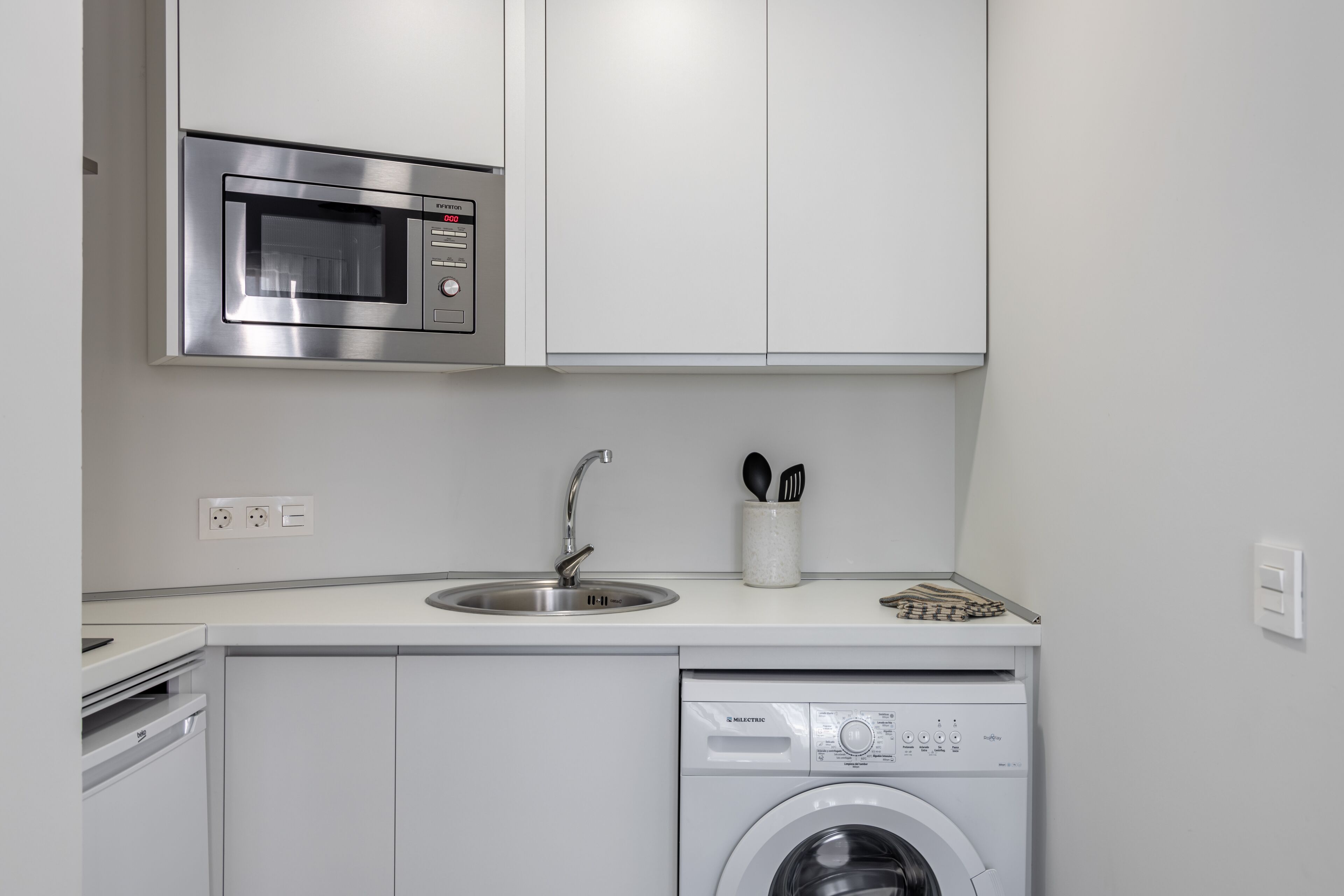 Uma cozinha compacta com micro-ondas embutido, pia e máquina de lavar roupas com abertura frontal.