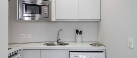 Uma cozinha compacta com micro-ondas embutido, pia e máquina de lavar roupas com abertura frontal.