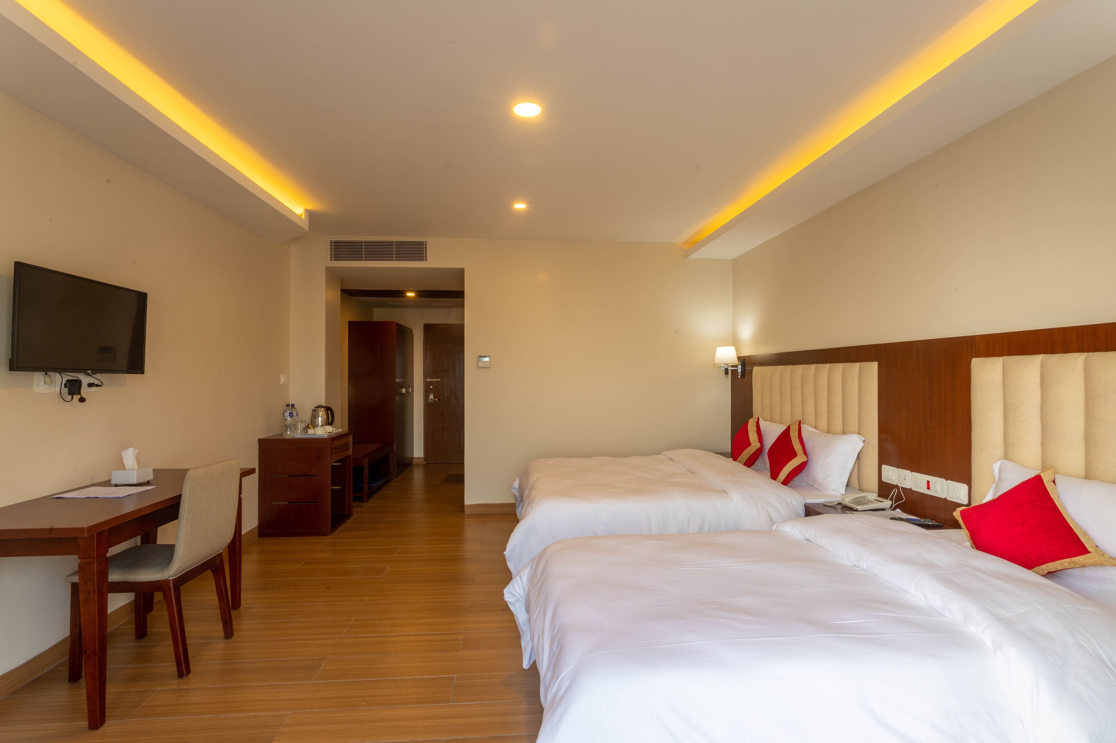 A hotel room with two beds, a desk with a chair, a television, and a kitchenette area.