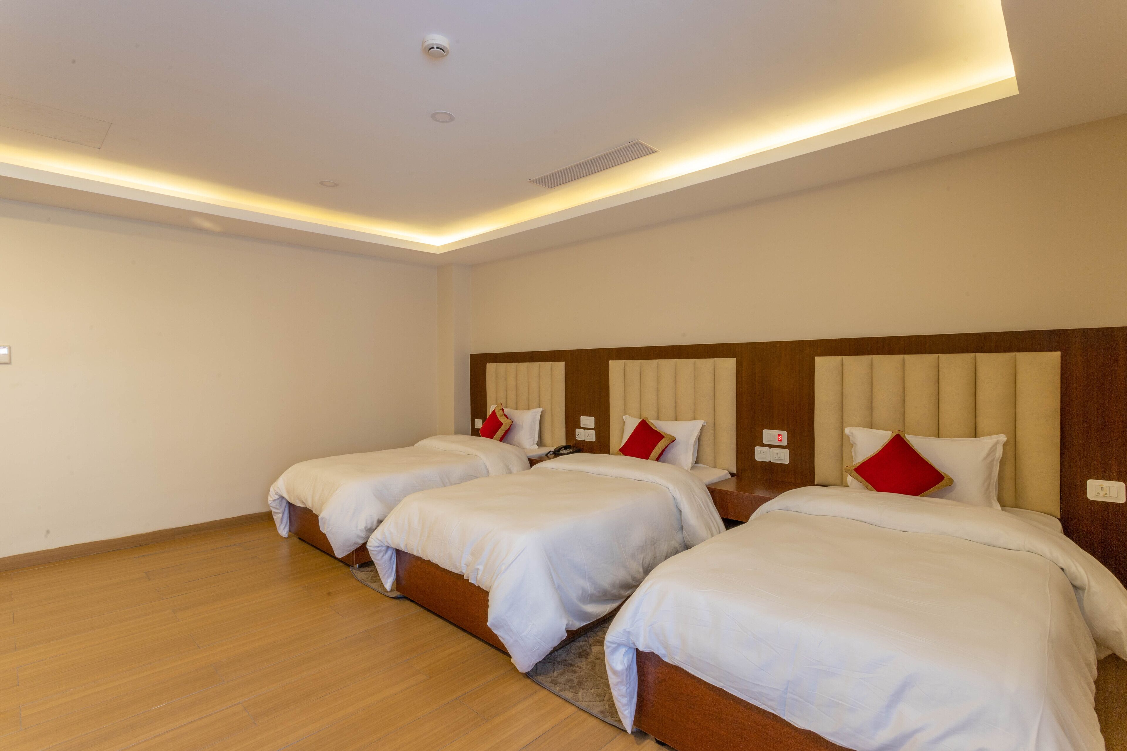 A hotel room with three single beds, wooden flooring, and a modern ceiling design.