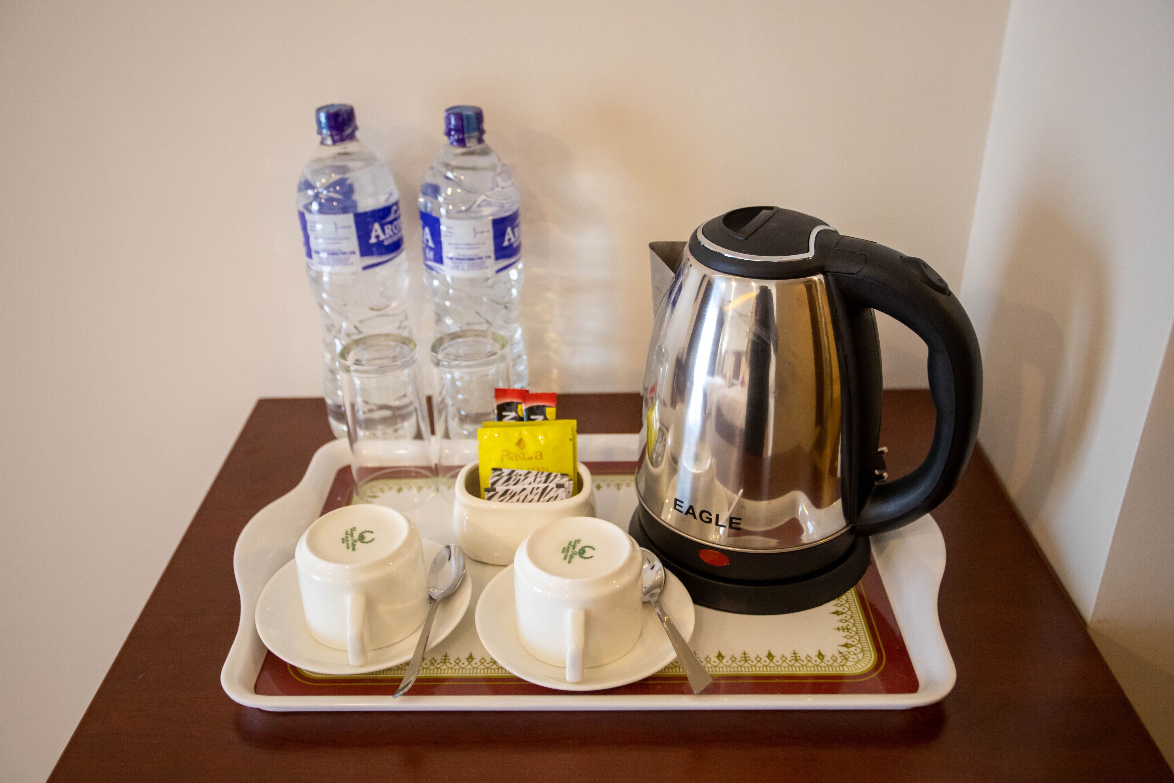 A tray with two water bottles, a coffee pot, and two cups with spoons on a table.