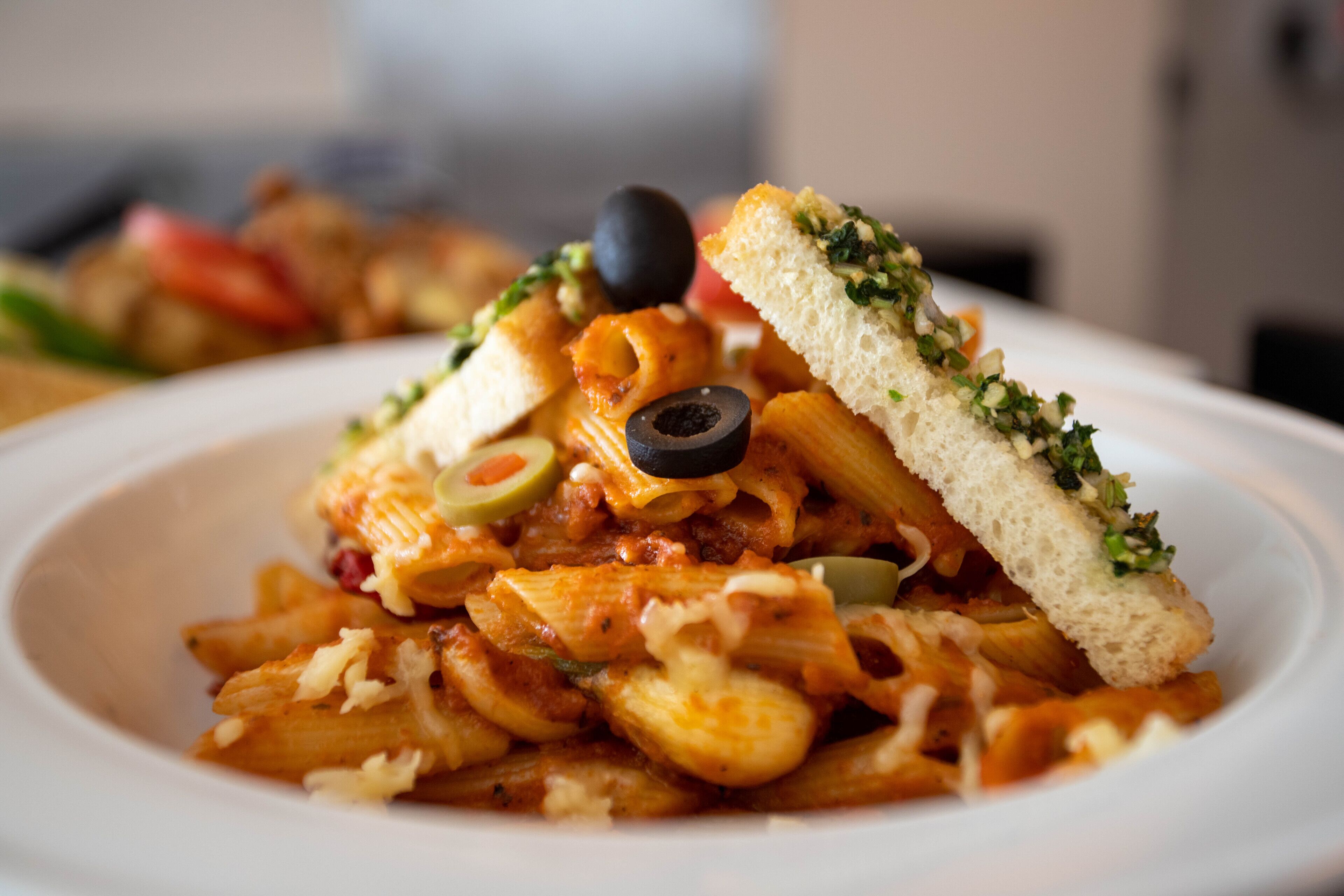 A plate of pasta with a slice of bread on top, garnished with olives and herbs.