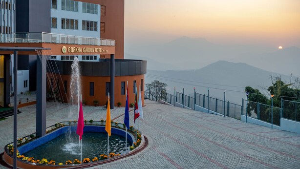 A hotel with a fountain, flags, and a mountainous backdrop.