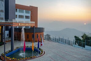 A hotel with a fountain, flags, and a mountainous backdrop.