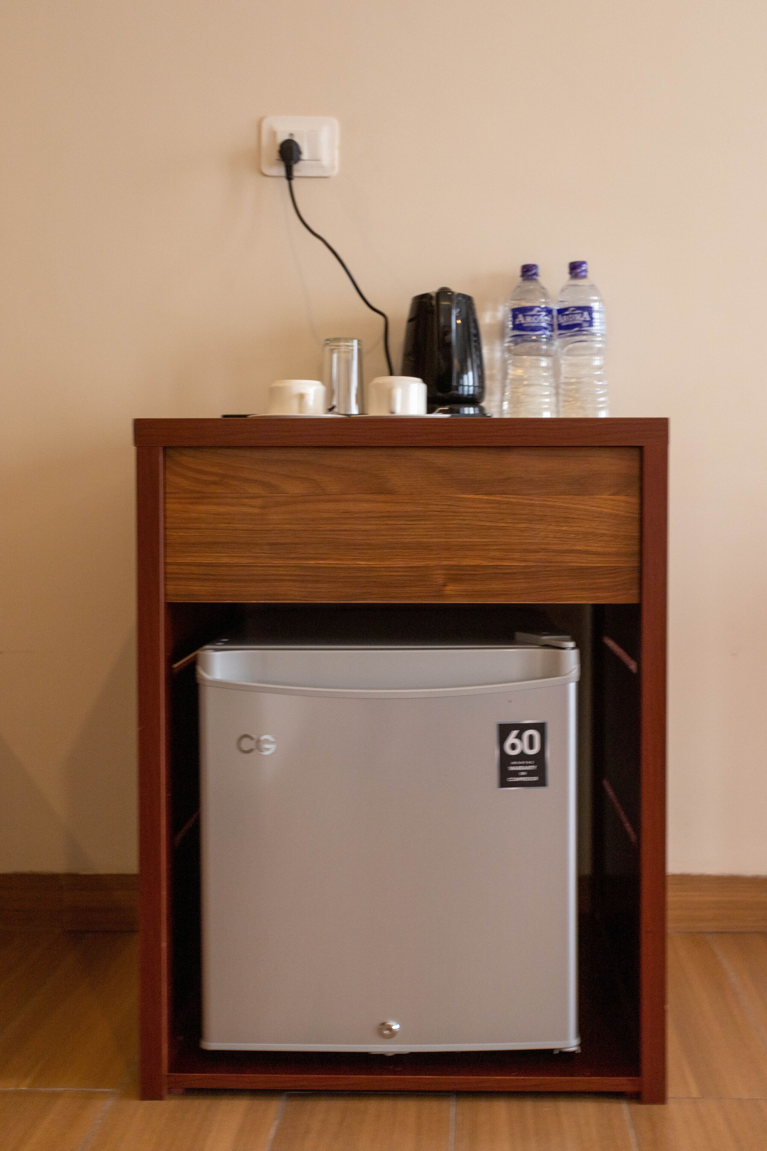 A compact kitchenette with a built-in refrigerator, a coffee maker, and two water bottles on a wooden cabinet.