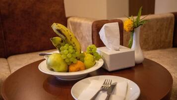 Una mesa de comedor con un frutero que contiene plátanos, uvas y manzanas, una caja de pañuelos y un plato con un tenedor y servilleta.