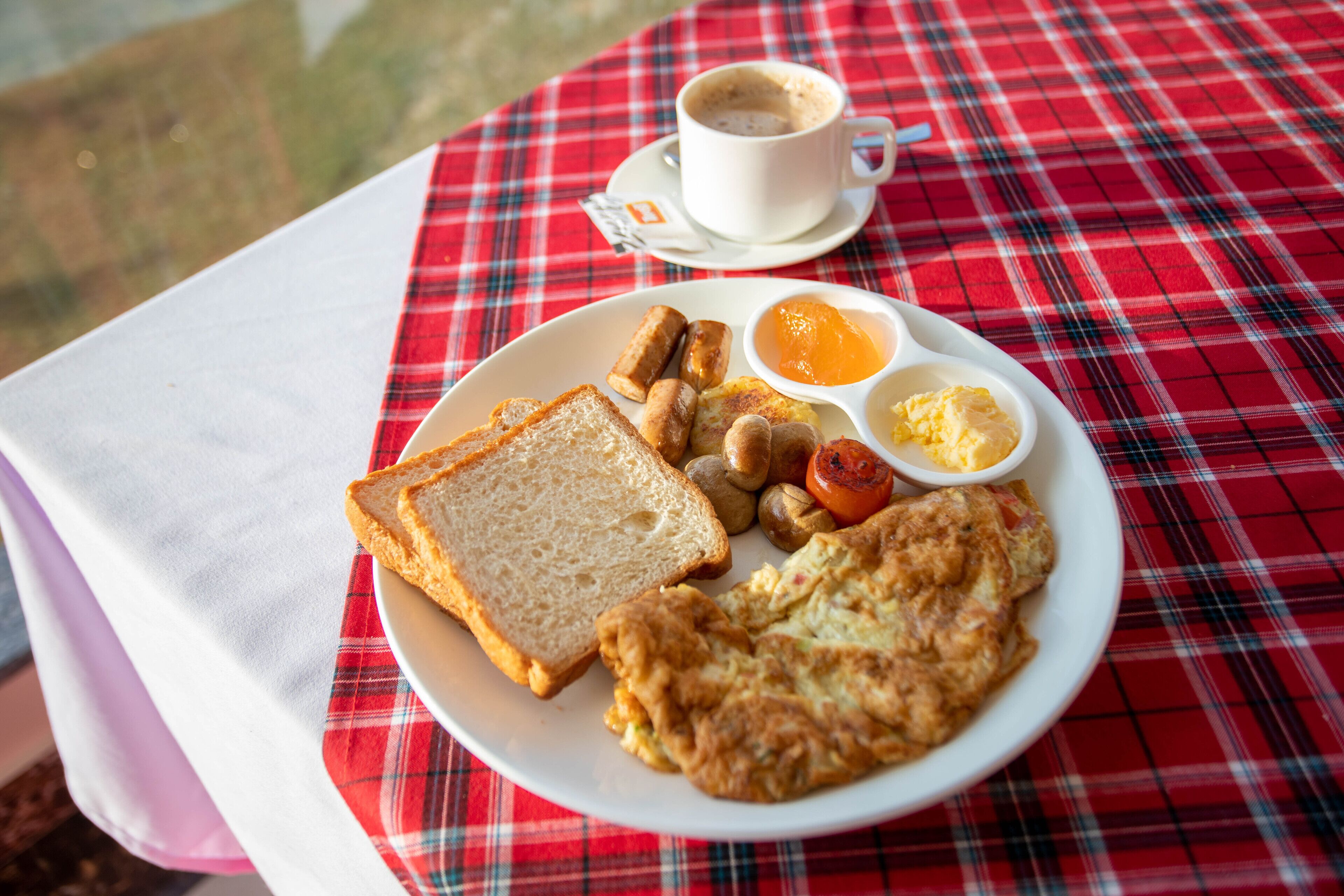 A breakfast plate with toast, eggs, sausages, and a cup of coffee on a red plaid tablecloth.