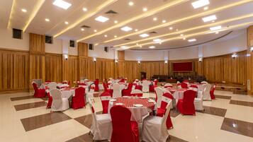 Un salón de banquetes con mesas y sillas redondas, paneles de madera en las paredes y un escenario al frente.