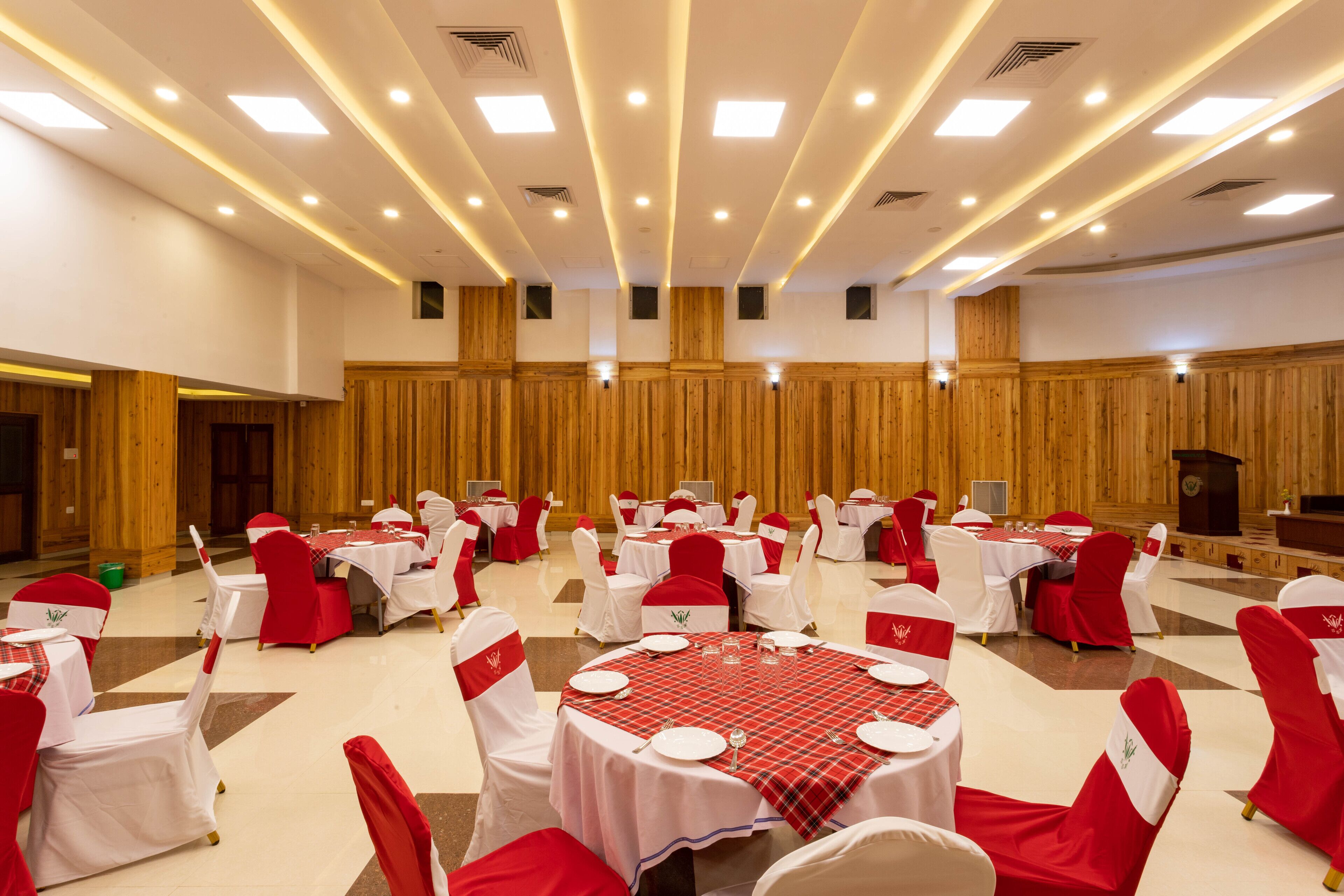 A banquet hall with round tables, red and white chairs, and a wooden panel wall.