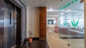 A modern lobby with a glass-fronted restaurant and bar, a reception desk, and a potted plant.