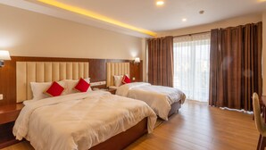 A hotel room with two beds, wooden headboard, beige walls, and a large window with curtains.