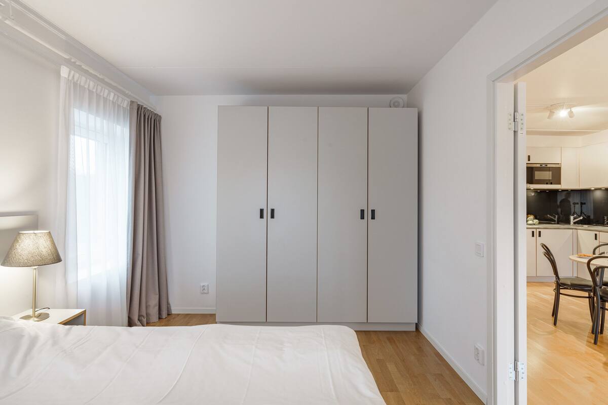 A bedroom with a bed, a nightstand, a lamp, and a wardrobe.