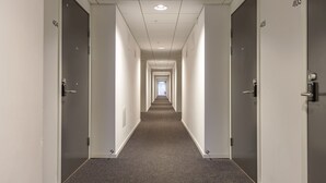 A long, narrow hallway with doors numbered 404 and 405 on either side, leading to a bright end. - Story Living Lidingö (Lidingo)