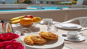 A table with fruits, pastries, and a view of a swimming pool and buildings. - Sunny Escape near Silver Beach for 3 (Alba Adriatica (TE))