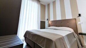 A modern hotel room with a large bed, a bedside table, a window with sheer curtains, and a striped wall design. - Sunny Escape near Silver Beach for 3 (Alba Adriatica (TE))