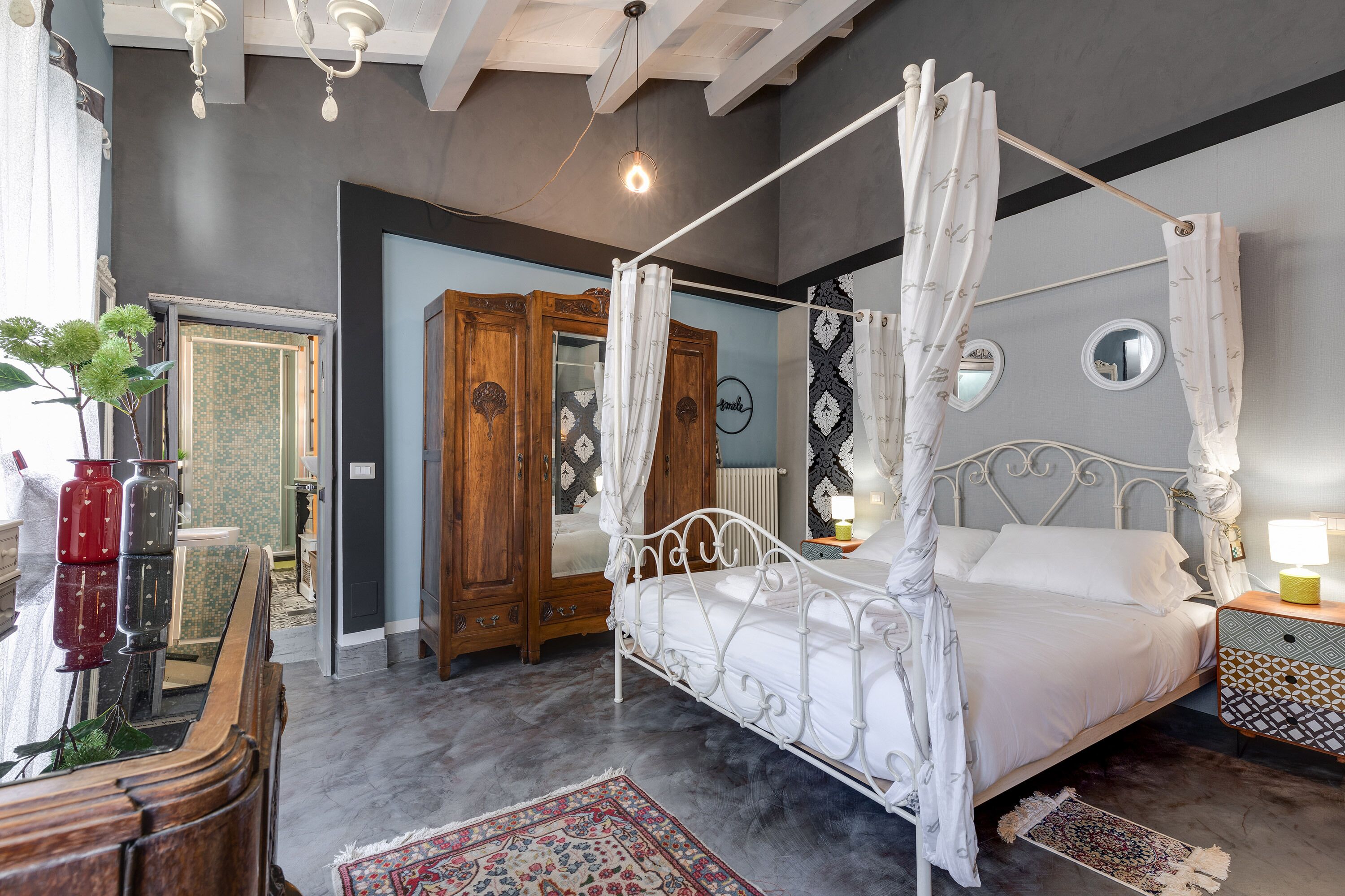 A four-poster canopy bed with a white canopy, a wooden wardrobe, a mirror, and a nightstand with a lamp.