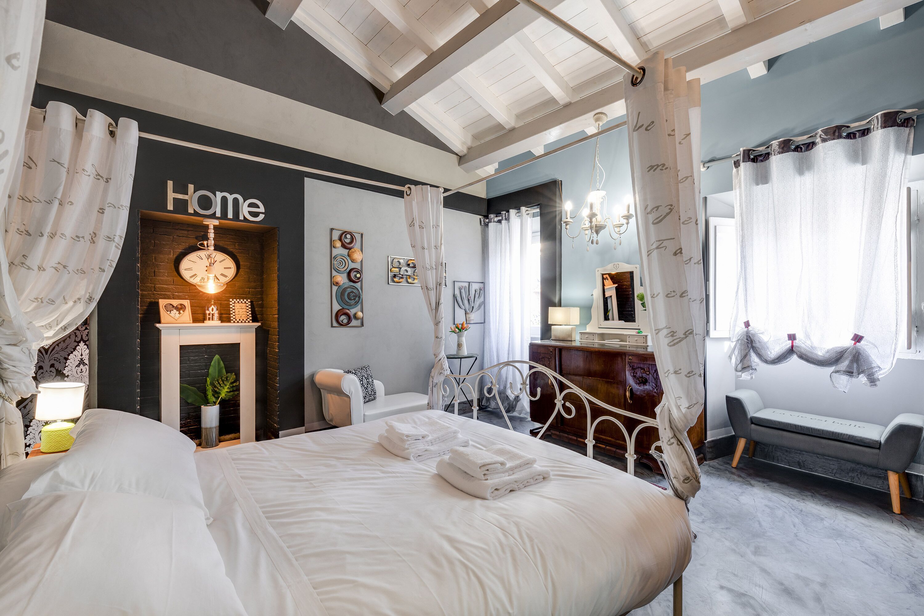 A bedroom with a bed, a bedside table with a lamp, a fireplace, and a window with curtains.
