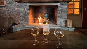 Una chimenea con una botella de vino y tres copas sobre una mesa de madera.