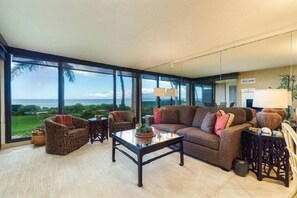 Enjoy a panoramic view of the lush landscape and ocean from this spacious living room with a comfortable seating area.