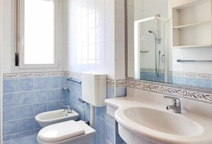 Bathroom features a toilet, bidet, and sink, with a window and mirror.