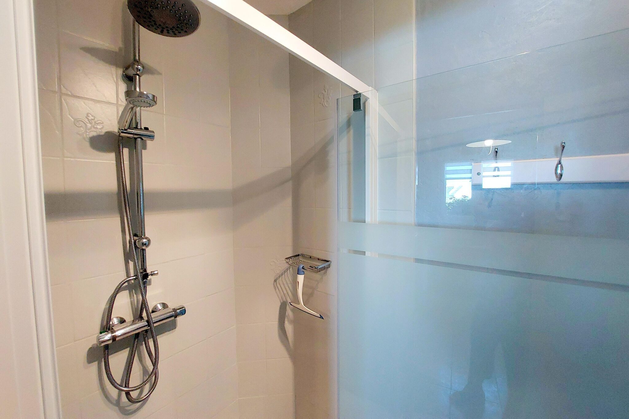 Une douche équipée d’un pommeau de douche à main et d’un robinet fixé au mur.