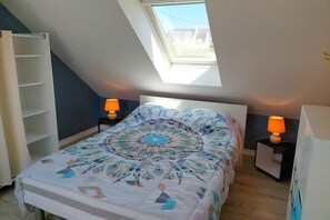 Ein Schlafzimmer mit Dachfenster, einem Bett mit gemustertem Überwurf, zwei Nachttischen mit Lampen und einem weißen Kleiderschrank.