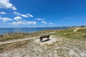 Un banc sur un sentier sablonneux, au bord d’une plage, sous un ciel dégagé.