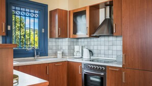 A kitchen with wooden cabinets, a stainless steel range hood, a built-in oven, and a window with a view of greenery. - Villa Rudi (Argostoli)