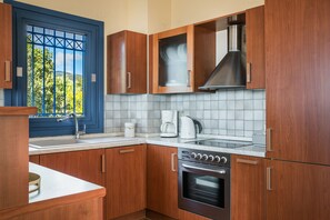 A kitchen with wooden cabinets, a stainless steel range hood, a built-in oven, and a window with a view of greenery.