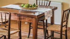 A dining area with a wooden table, chairs, a bowl of fruit, and a window with sheer curtains. - Villa Rudi (Argostoli)