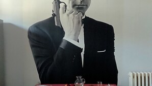 Ein Mann in einem Anzug hält eine Waffe an einem Tisch mit Tellern, einem Krug und Gläsern.