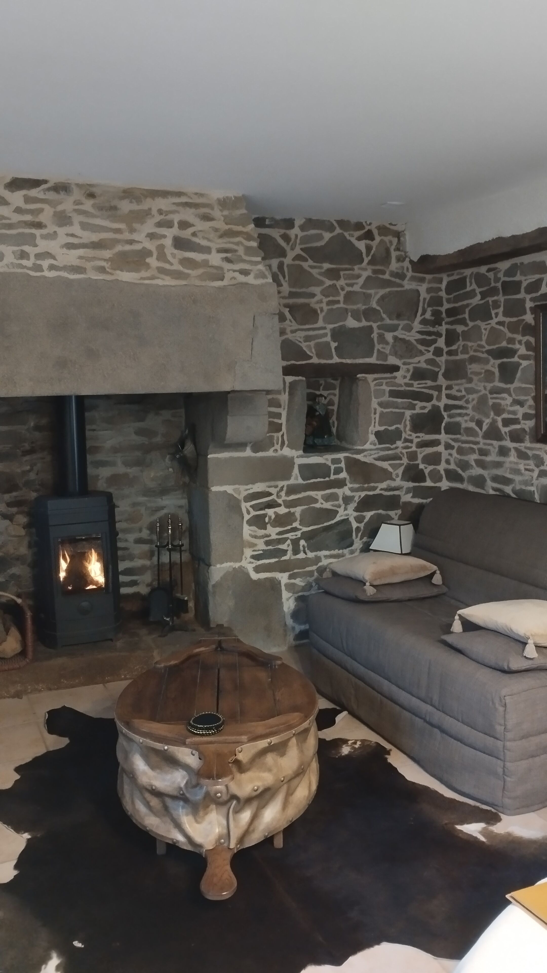 A cozy living room with a stone wall, a fireplace, a sofa, and a round wooden table.