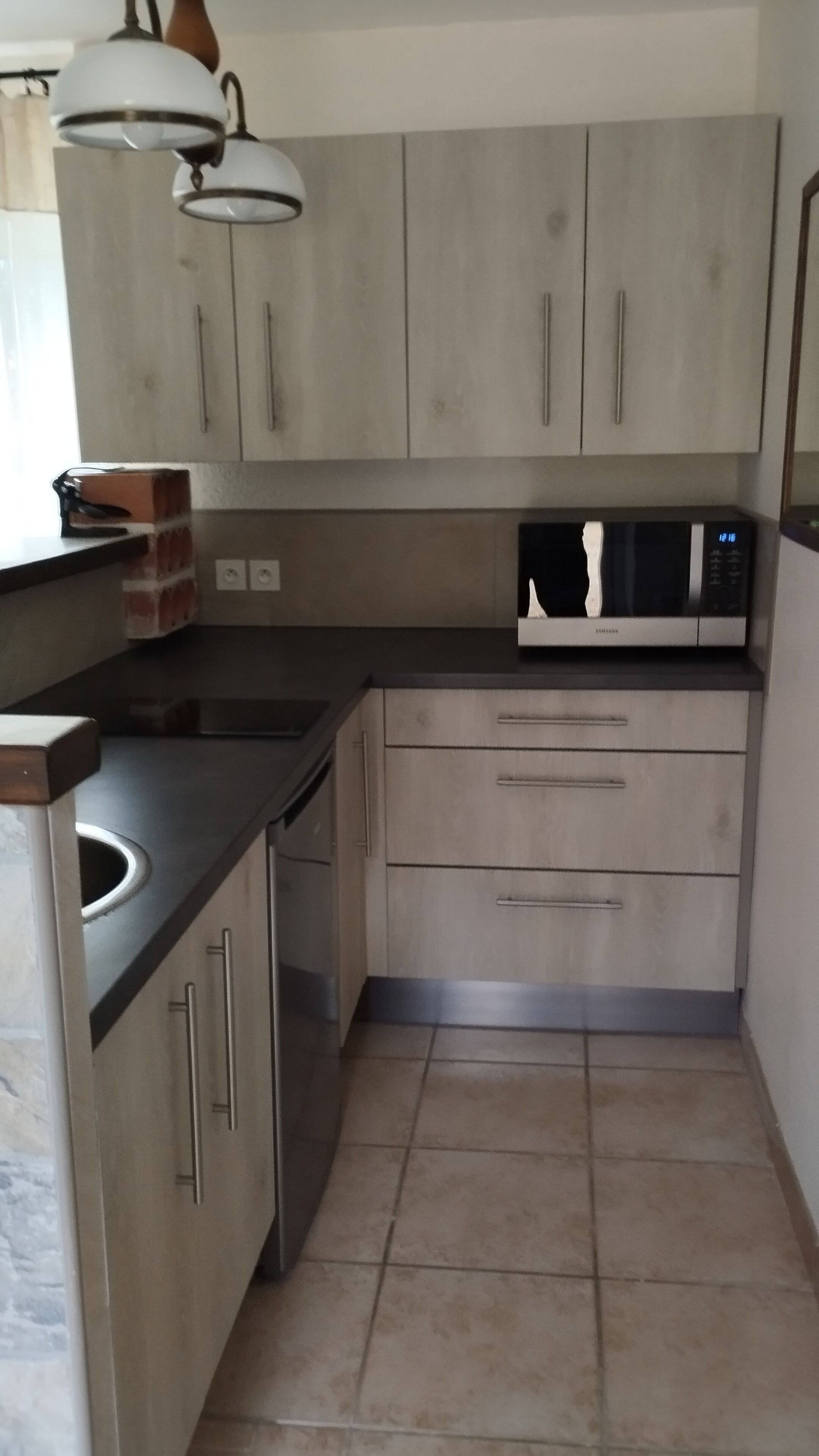 Een kleine keuken met grijze kastjes, een magnetron en een spoelbak.