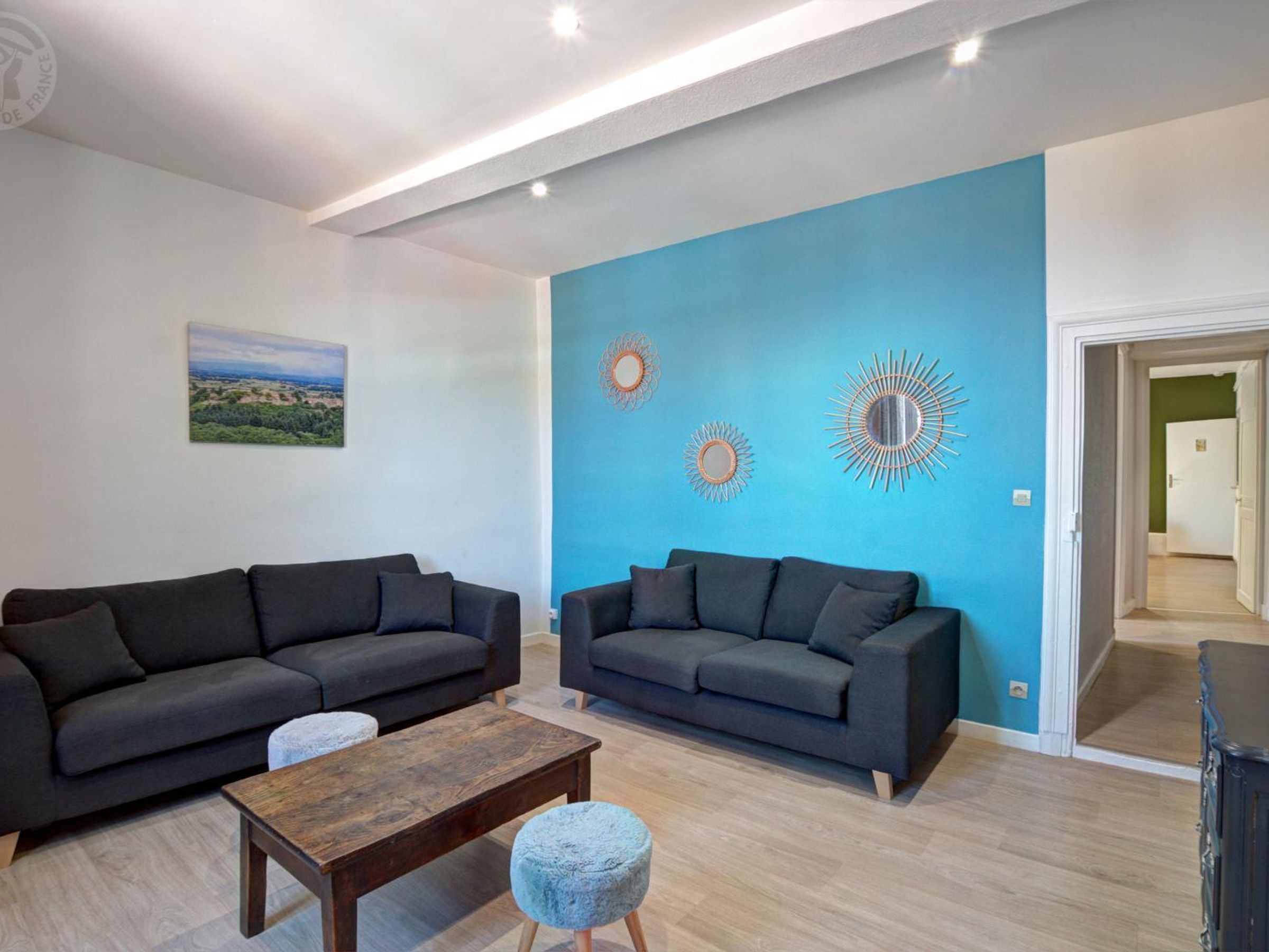 A living room with two dark sofas, a wooden coffee table, and a blue accent wall with decorative mirrors.