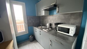 A compact kitchen with grey cabinets, a white microwave, a coffee maker, and a window with a view of a brick building.