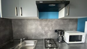 A kitchen with grey cabinets, a stainless steel sink, a gas stove, a coffee maker, and a white microwave.