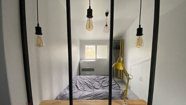 A bedroom with a bed, a desk, and a mirror reflecting the room.