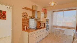 A modern kitchen with white cabinets, a wooden countertop, and a built-in oven. There is a window with blinds, a hanging light fixture, and a clock on the wall.