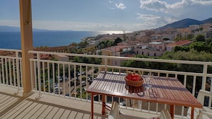 A balcony with a table and chairs, overlooking a coastal town with buildings and a view of the sea.