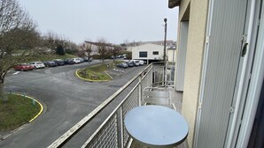 A balcony with a small table and a view of a parking lot with several cars and a building in the background. - Central Apartment with Balcony, Wi-Fi & Dishwasher - Near Shops & Spa (La Roche-Posay)