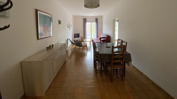 A spacious dining area with a long table and chairs, a kitchen counter with cabinets, and a large window with curtains. - Central Apartment with Balcony, Wi-Fi & Dishwasher - Near Shops & Spa (La Roche-Posay)