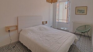 A bedroom with a bed, a hanging light fixture, a window, a radiator, and a chair. - Ajaccio: Charming 2BR, 4 guests, Wifi, Downtown (Ajaccio)