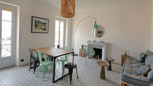 A living room with a dining table, chairs, a sofa, a fireplace, and a hanging light fixture. - Ajaccio: Charming 2BR, 4 guests, Wifi, Downtown (Ajaccio)