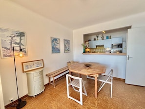 Une cuisine compacte équipée d’un four à micro-ondes, d’un petit réfrigérateur et d’un meuble blanc. On y trouve une table en bois avec des chaises, un banc et un lampadaire.